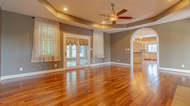 empty room featuring a raised ceiling, ceiling fan with notable chandelier, and light wood-type flooring