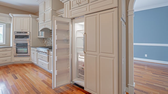 kitchen featuring tasteful backsplash, ornamental molding, appliances with stainless steel finishes, and light wood-type flooring