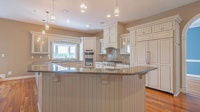 kitchen featuring stainless steel appliances, light hardwood / wood-style floors, decorative light fixtures, and a breakfast bar