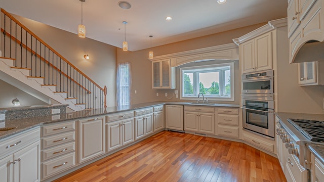 kitchen featuring light hardwood / wood-style floors, decorative light fixtures, stone countertops, stainless steel double oven, and sink