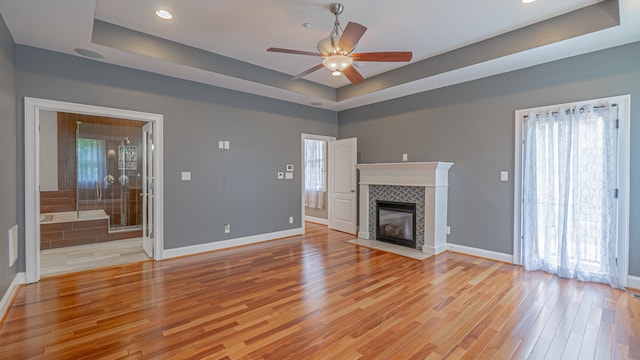 unfurnished living room with light hardwood / wood-style floors, a tile fireplace, a tray ceiling, and ceiling fan