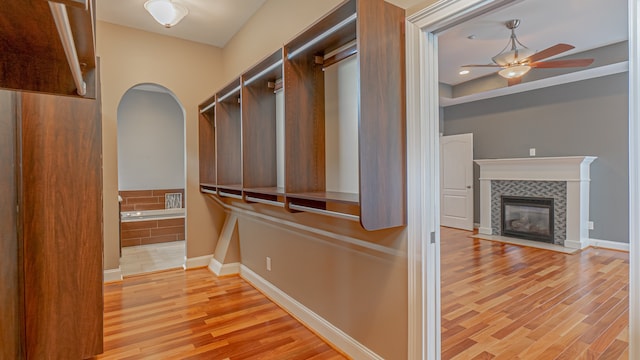 walk in closet with ceiling fan, a tile fireplace, and light wood-type flooring