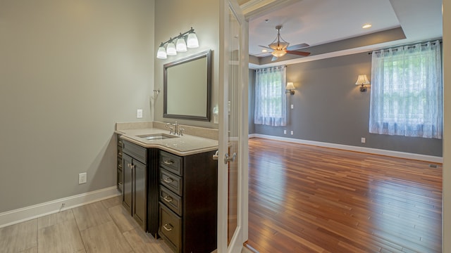 bathroom with hardwood / wood-style flooring, a raised ceiling, ceiling fan, and vanity