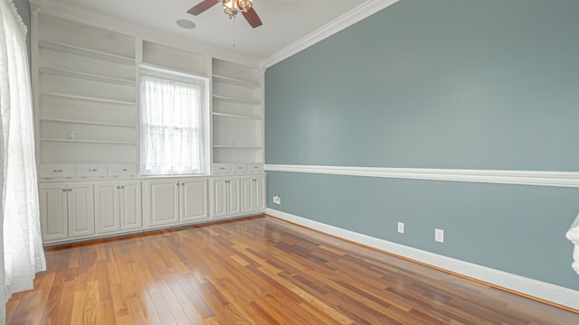 unfurnished room with crown molding, ceiling fan, built in shelves, and light hardwood / wood-style flooring