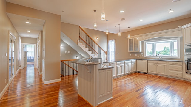 kitchen with hanging light fixtures, light wood-type flooring, a kitchen bar, sink, and oven