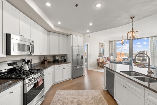 kitchen with dark stone counters, light hardwood / wood-style floors, stainless steel appliances, a notable chandelier, and pendant lighting