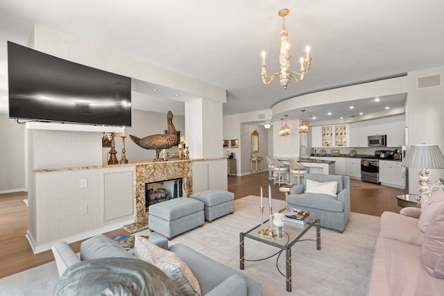 living room featuring a premium fireplace, an inviting chandelier, and light hardwood / wood-style flooring