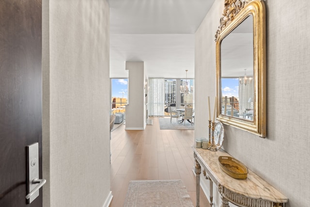 corridor with an inviting chandelier, a wealth of natural light, and light wood-type flooring