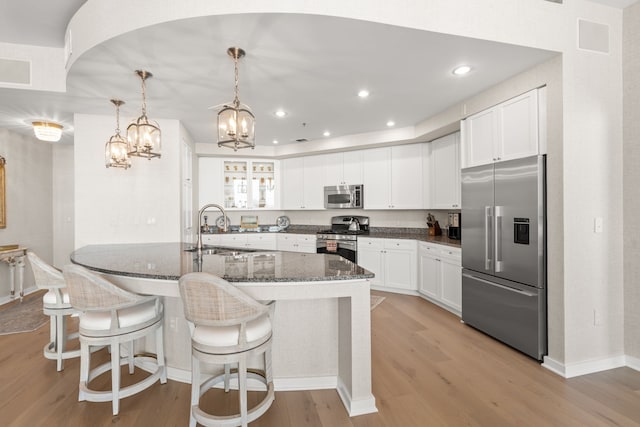 kitchen with pendant lighting, light hardwood / wood-style flooring, appliances with stainless steel finishes, dark stone countertops, and sink