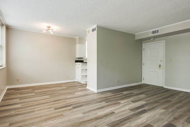 empty room with a textured ceiling, crown molding, and wood-type flooring