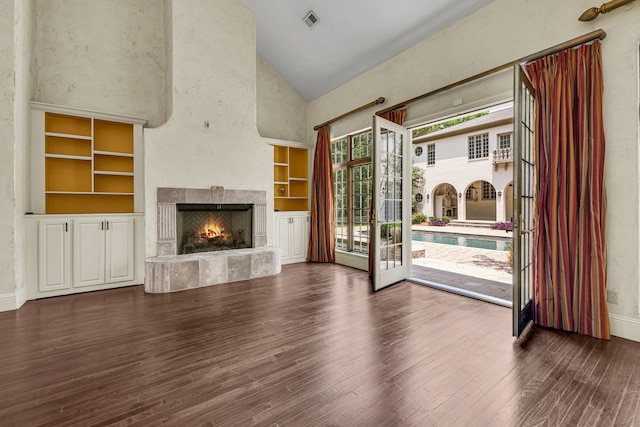 unfurnished living room featuring hardwood / wood-style flooring, built in features, a stone fireplace, high vaulted ceiling, and french doors