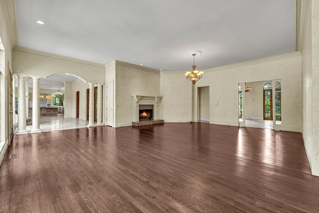 unfurnished living room with a premium fireplace, an inviting chandelier, dark wood-type flooring, ornamental molding, and ornate columns