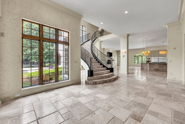 foyer entrance featuring decorative columns, ornamental molding, and an inviting chandelier