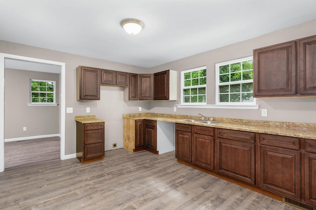 kitchen featuring sink, light stone counters, light hardwood / wood-style floors, and a healthy amount of sunlight