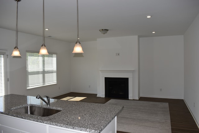 kitchen with hanging light fixtures, dark hardwood / wood-style flooring, dark stone countertops, and sink