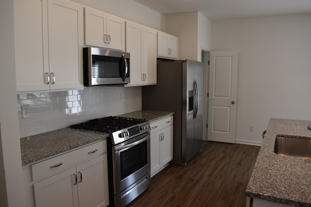 kitchen with appliances with stainless steel finishes, dark stone counters, dark wood-type flooring, backsplash, and white cabinets