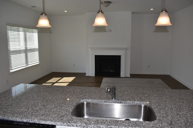 kitchen with light stone countertops, decorative light fixtures, sink, and dark hardwood / wood-style flooring