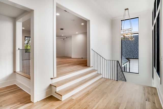 staircase with plenty of natural light, light hardwood / wood-style floors, and a notable chandelier