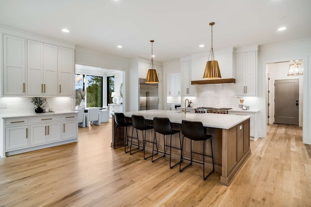 kitchen with an island with sink, light hardwood / wood-style flooring, built in fridge, white cabinetry, and backsplash