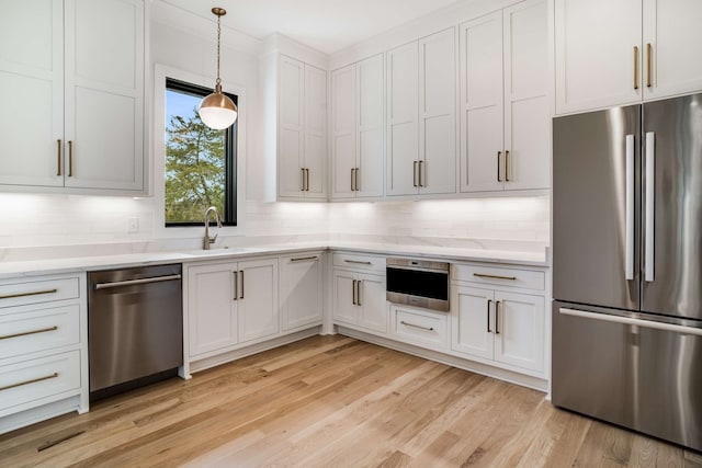 kitchen with white cabinets, light hardwood / wood-style floors, stainless steel appliances, and decorative light fixtures