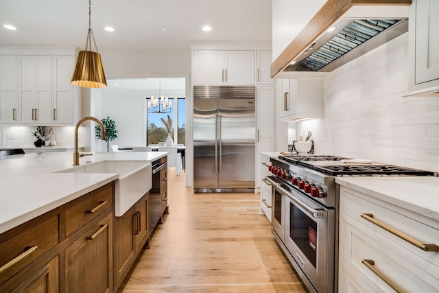 kitchen with pendant lighting, premium range hood, tasteful backsplash, high quality appliances, and light wood-type flooring