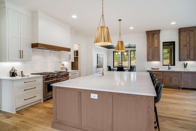 kitchen featuring a kitchen island with sink, tasteful backsplash, white cabinetry, and double oven range