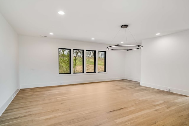 empty room with a notable chandelier and light hardwood / wood-style floors