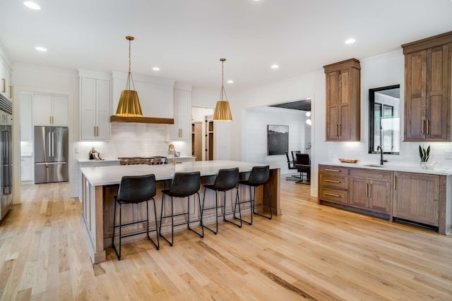 kitchen featuring stainless steel refrigerator, white cabinetry, an island with sink, light hardwood / wood-style flooring, and backsplash