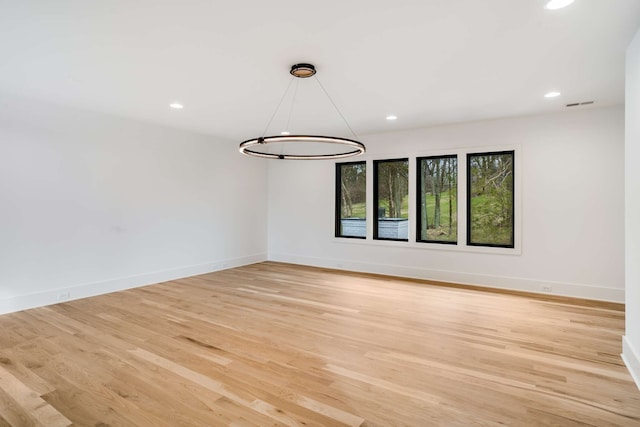 unfurnished room featuring an inviting chandelier and light wood-type flooring