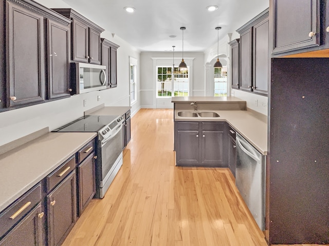 kitchen featuring decorative light fixtures, stainless steel appliances, sink, and light wood-type flooring