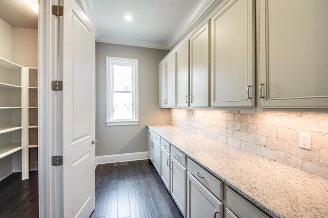 kitchen with backsplash, ornamental molding, light stone counters, and dark hardwood / wood-style flooring