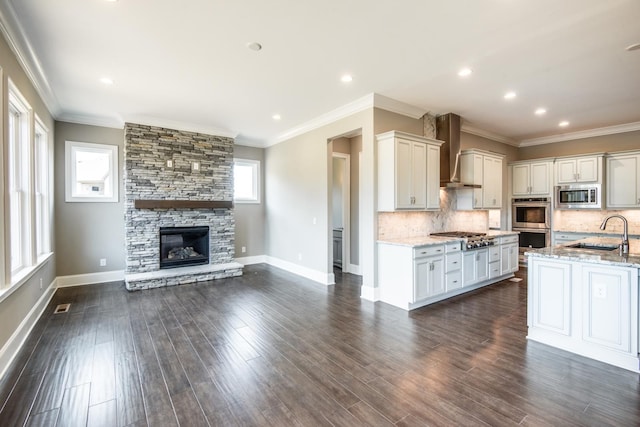 kitchen with sink, backsplash, stainless steel appliances, light stone countertops, and wall chimney range hood