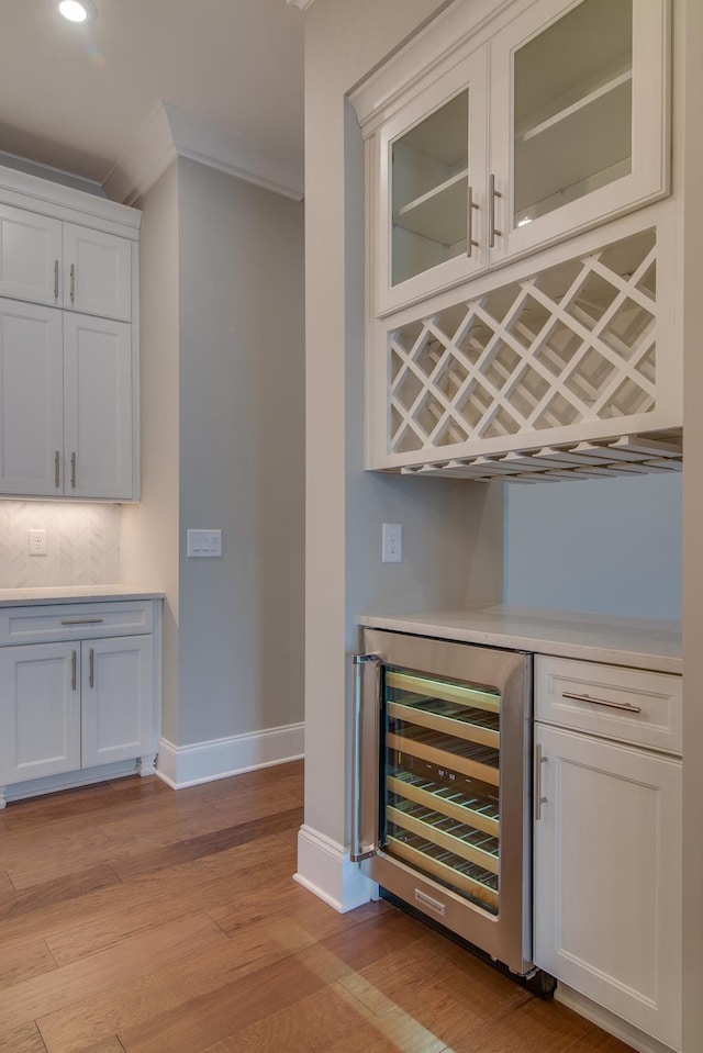 bar with light hardwood / wood-style flooring, wine cooler, white cabinets, tasteful backsplash, and crown molding