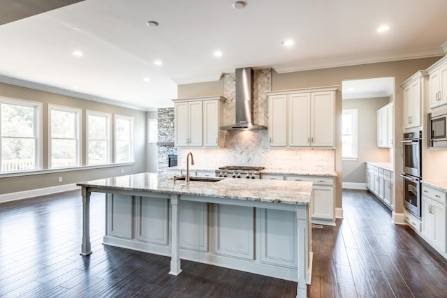 kitchen with wall chimney exhaust hood, a kitchen island with sink, sink, and dark wood-type flooring