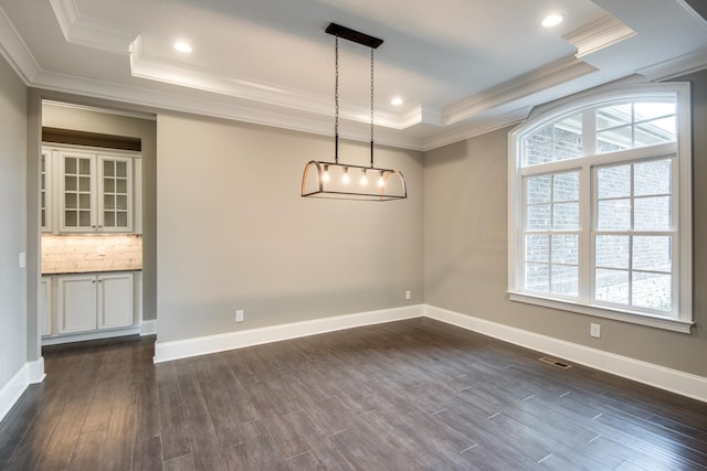 unfurnished dining area with a tray ceiling, ornamental molding, and dark wood-type flooring