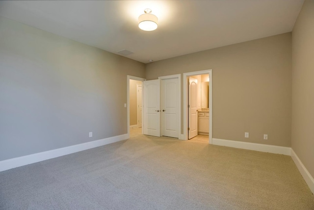 unfurnished bedroom featuring a closet, connected bathroom, and light colored carpet