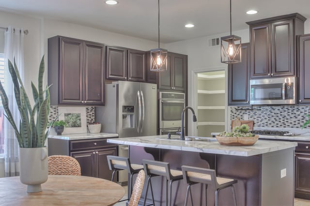 kitchen with decorative light fixtures, a center island with sink, appliances with stainless steel finishes, and tasteful backsplash