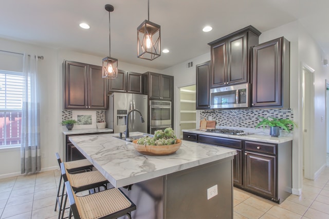 kitchen with appliances with stainless steel finishes, tasteful backsplash, a center island with sink, and a kitchen breakfast bar