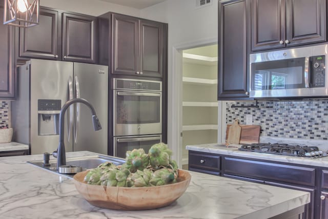 kitchen with backsplash, dark brown cabinets, appliances with stainless steel finishes, and light stone counters