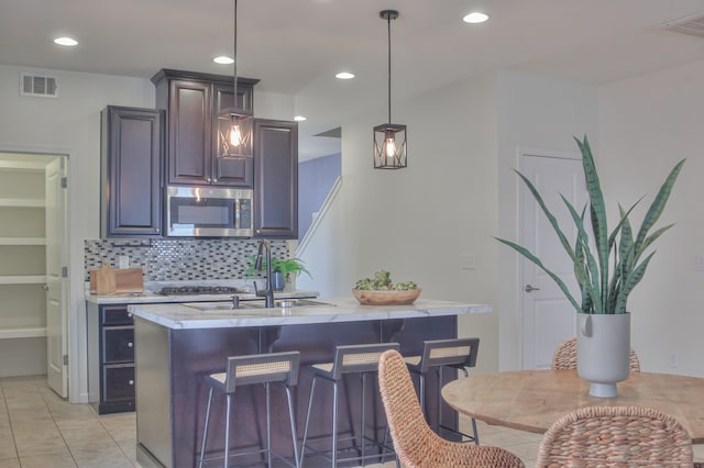 kitchen with light tile flooring, pendant lighting, a breakfast bar area, backsplash, and sink