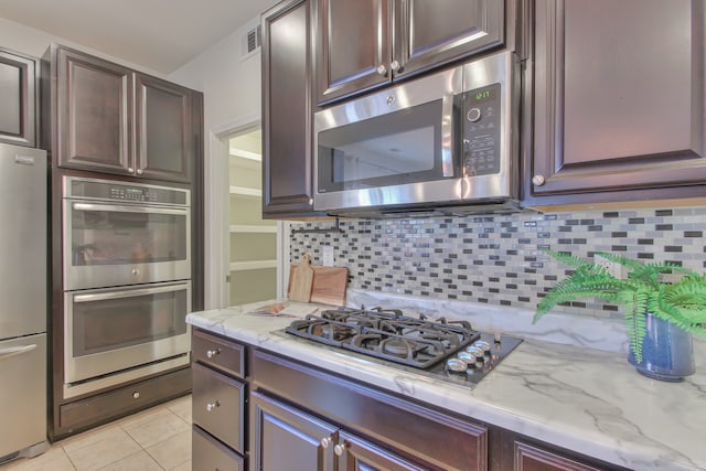 kitchen with backsplash, appliances with stainless steel finishes, light tile floors, light stone counters, and dark brown cabinets