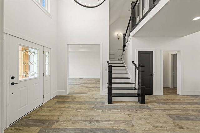 entrance foyer featuring a towering ceiling, an inviting chandelier, hardwood / wood-style flooring, and plenty of natural light