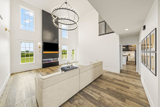 living room featuring a large fireplace, dark hardwood / wood-style floors, a chandelier, and a high ceiling