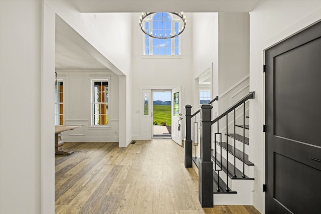 entryway featuring a notable chandelier, a towering ceiling, and light hardwood / wood-style flooring