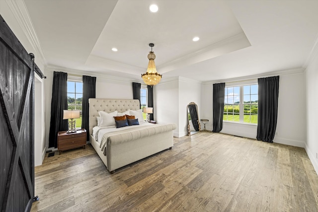 bedroom featuring a barn door, a raised ceiling, a chandelier, and light wood-type flooring