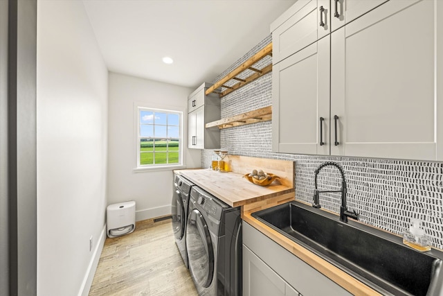 clothes washing area featuring sink, cabinets, washer and clothes dryer, and light hardwood / wood-style floors