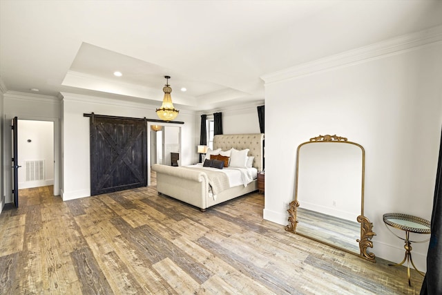 unfurnished bedroom with crown molding, a barn door, wood-type flooring, and a tray ceiling