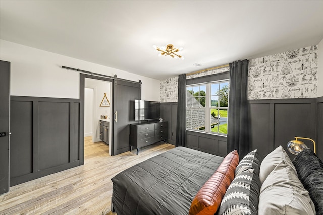 bedroom featuring a barn door, light wood-type flooring, and ensuite bathroom