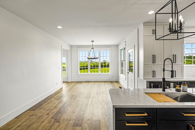 kitchen with pendant lighting, an inviting chandelier, light stone countertops, light hardwood / wood-style flooring, and sink