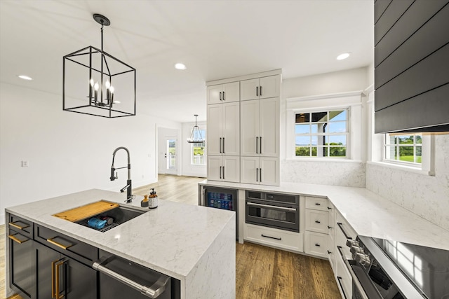 kitchen with a center island with sink, dark hardwood / wood-style floors, stainless steel range, light stone countertops, and sink